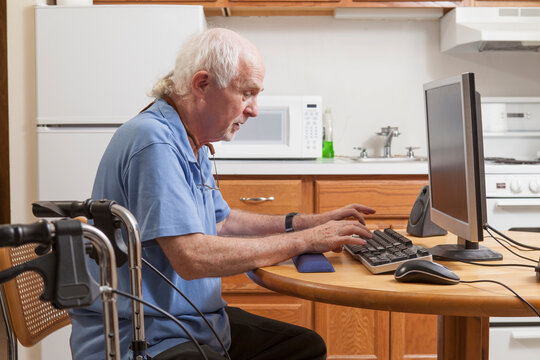 Man with Ataxia with his walker working on his computer in the kitchen
