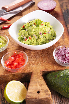 fresh homemade guacamole bowl with ingredients on wooden board