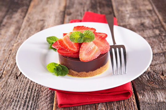 chocolate tartlet with fresh strawberry slices and mint on plate