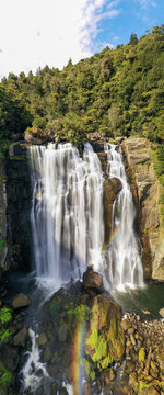 Aerial view of Marokopa Falls cascading down rocky cliffs surrounded by lush green forest with a faint rainbow in the mist Te Anga, Waikato Region, New Zealand.