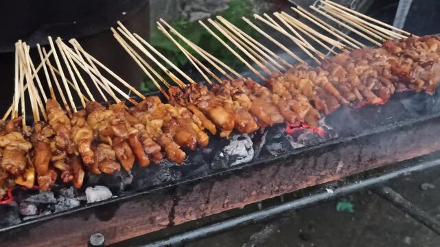 Satay being grilled over coconut shell charcoal, producing traditional smoky aromas and authentic flavors in a classic outdoor cooking process.