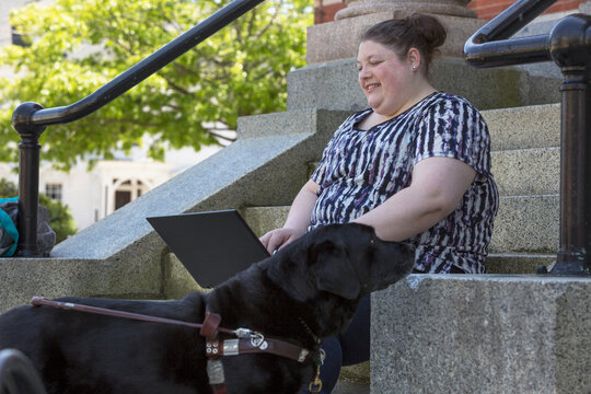 Woman with Visual Impairment sitting with her service dog and using a computer