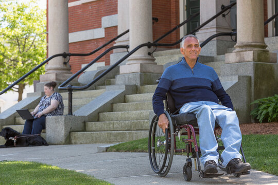 Man with Spinal Cord Injury sitting in wheelchair with his daughter in background who is Blind