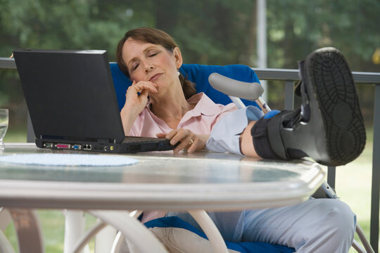 Woman with a boot on her foot napping on a chair in front of a laptop
