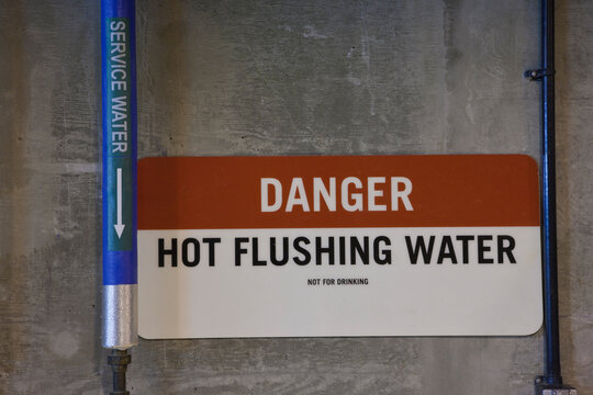 Hot flushing water pipe with warning sign in a sewage treatment plant