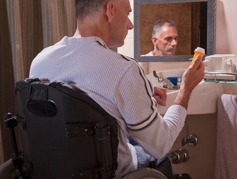 Man with spinal cord injury in a wheelchair looking at a pill bottle