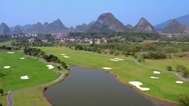 A well-maintained golf course with water hazards and sand bunkers, set against distinctive karst mountains under a clear blue sky.