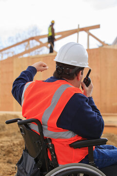 Man in a wheelchair uses a walkie talkie on a construction site