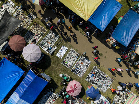 Aerial view of Bonyokan Pasar Legi with people walking between colorful tarps and goods displayed on mats in Kecamatan Jatinom, Jawa Tengah, Indonesia.