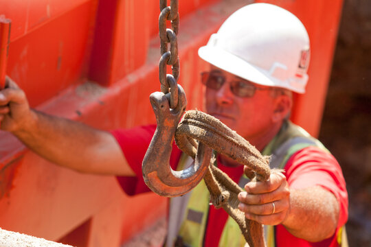 Construction worker placing lifting strap on hook