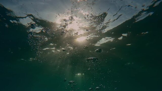 Sea waves and bright sunshine on water, trickle of air bubbles slowly rising to the surface in morning light (golden hour) backlighting by vivid sunbeams, natural marine background