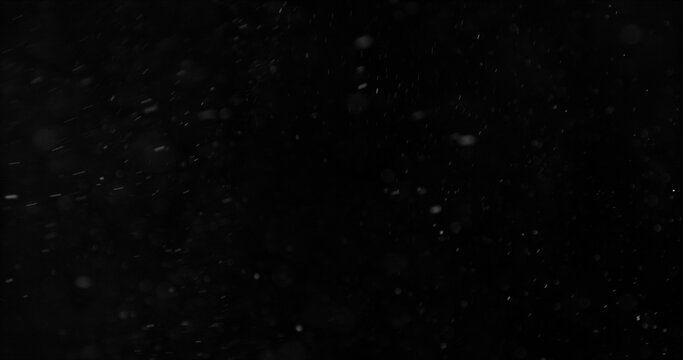 Realistic falling snow and airborne dust particles drifting through dark space. Atmospheric winter storm effect on black background, ideal for overlays, VFX compositing and cinematic scenes.