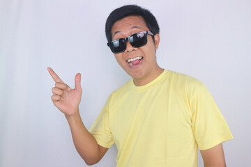 Naklejka premium Happy Asian Man wearing Sunglasses pointing Side showing, or recommending a product