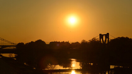 Naklejka premium An autumn sunset over the river and the silhouette of the footbridge.