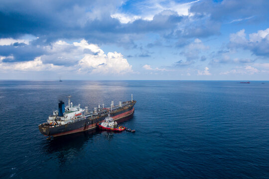 Aerial view of a large oil tanker ship on the blue sea with a small tugboat alongside under a cloudy sky Indonesia.