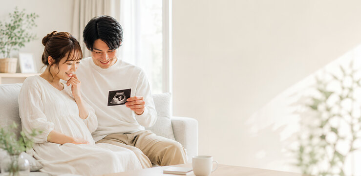 妊娠を喜びエコー写真を見つめる夫婦と明るいリビング