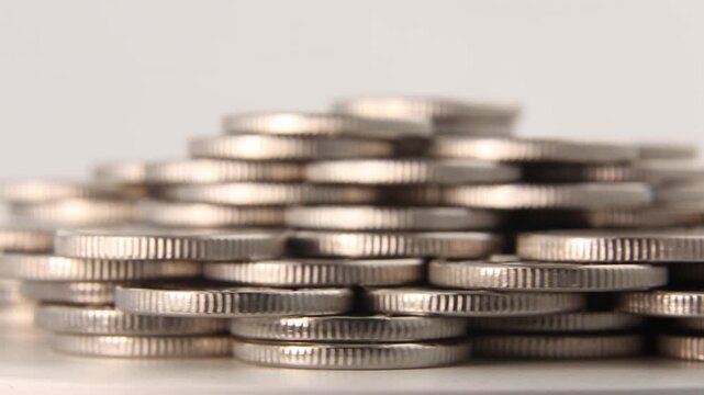 The camera opens with an extreme close-up of the ribbed edges of a silver coin spinning, revealing a large stack of coins in a full pyramid against a neutral light background in a studio setting.