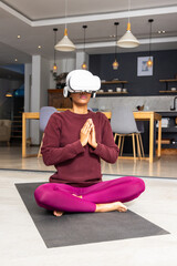 Fototapeta premium Person is meditating while wearing white VR headset on black yoga mat in open-plan kitchen