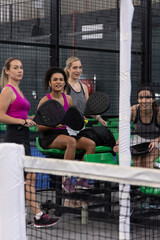 Obraz premium Diverse female teammates wearing sport tanks holding paddles resting on green bench at paddle court