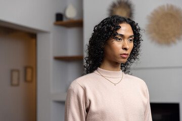 Obraz premium Non-binary person standing in living room wearing pale pink sweater, gold necklace, sunburst decor