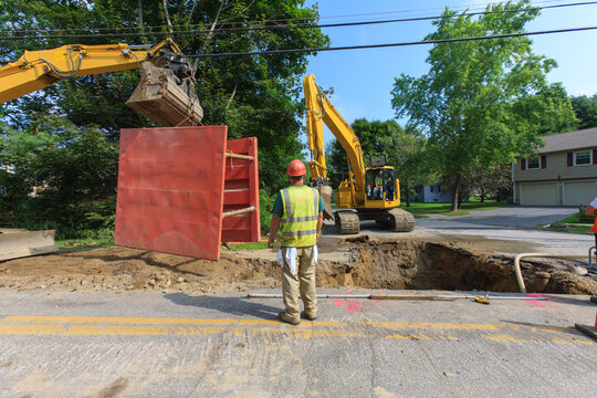 Construction worker watching excavator moving shoring to new section of project