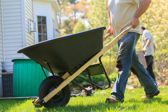 Landscaper moving wheelbarrow around a house