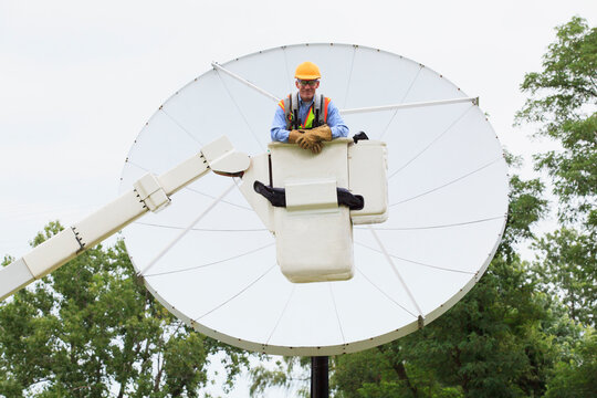 Communications engineer in bucket on truck in front of satellite dish