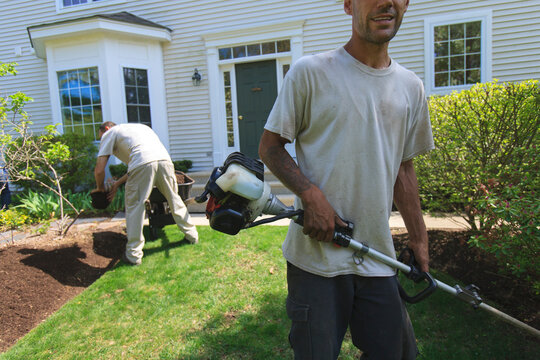 Landscapers working in a garden, one doing mulching and one doing edging with a power edger
