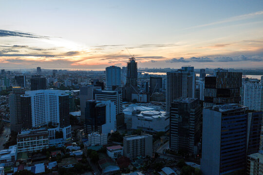 Aerial view of the modern skyline featuring skyscrapers and construction cranes under a sunset sky with the sea in the distance in Cebu City, Central Visayas, Philippines.