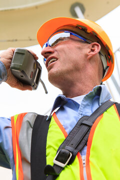 Engineer at electric power plant standing at satellite antenna dish while on walkie-talkie
