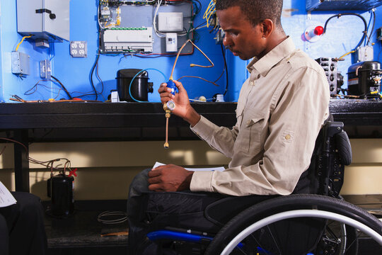Student in wheelchair examining air conditioner high pressure line in HVAC classroom