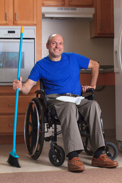 Man with Friedreich's Ataxia and deformed hands cleaning his house from his wheelchair with a broom