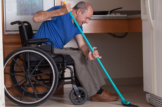 Man with Friedreich's Ataxia and deformed hands cleaning his house from his wheelchair with a broom