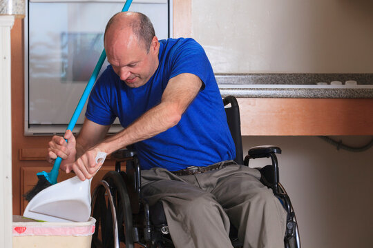 Man with Friedreich's Ataxia and deformed hands cleaning his house from his wheelchair with a broom