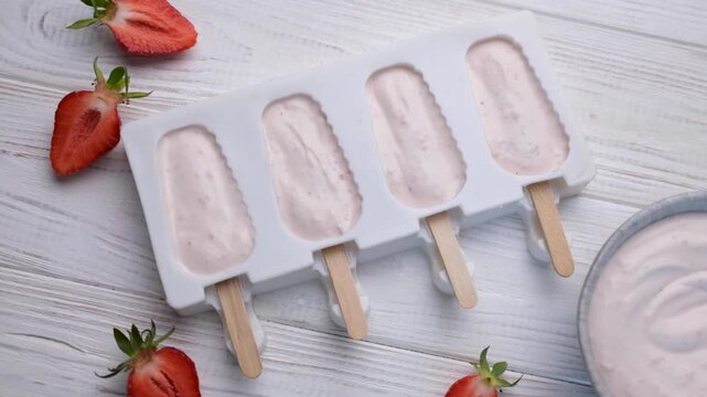 Preparing homemade strawberry yogurt popsicles on a table