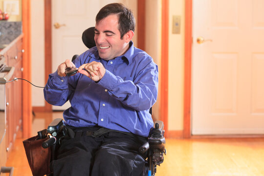 Man with Cerebral Palsy in his motorized wheelchair in his kitchen unplugging his cell phone