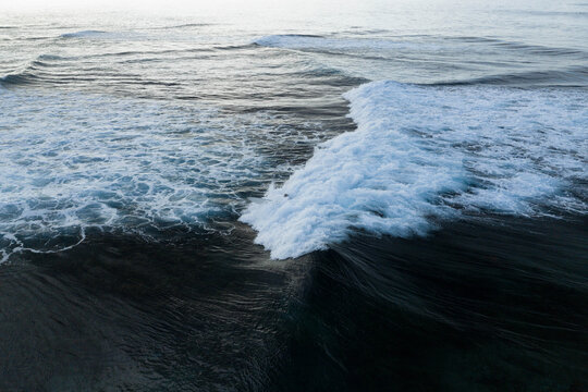 Aerial view of ocean waves breaking with white foam and ripples on the dark blue sea surface off the coast of Siargao Island General Luna, Caraga, Philippines.