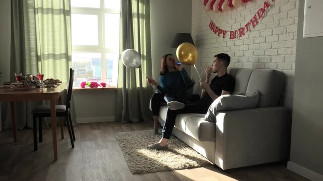 Mother and son playing with party horns while sitting on the sofa