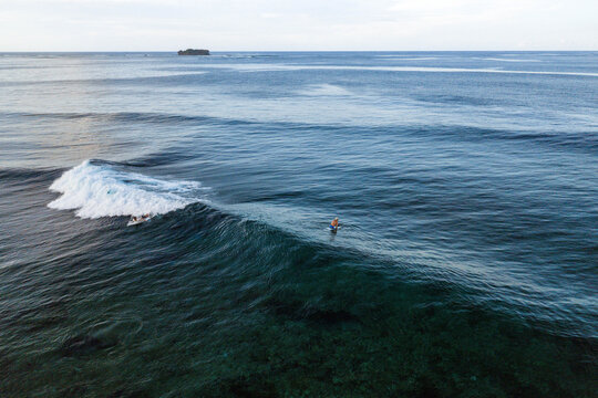 Aerial view of surfers riding a breaking wave in the clear blue ocean near Siargao Island General Luna, Caraga, Philippines.