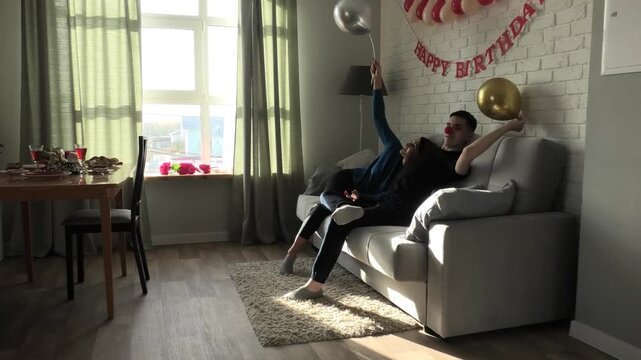 Son fixes golden balloon while sitting on sofa with mom