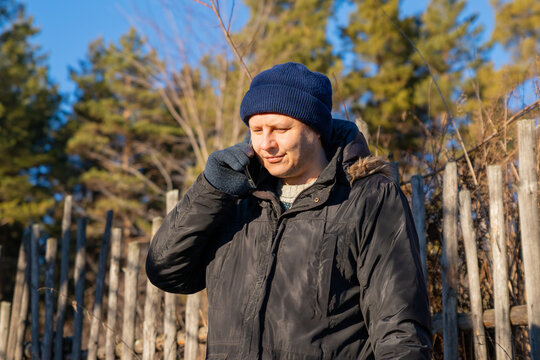 Man wearing winter clothes talking on a mobile phone outdoors. Casual young guy using smartphone for a conversation in nature. Cold weather communication and technology connectivity concept.