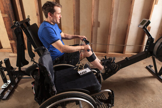Man with spinal cord injury using his rowing machine with a muscle stimulator attached