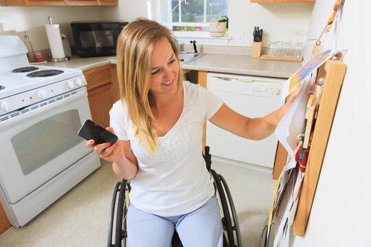 Woman with spinal cord injury in her accessible kitchen looking at notice board
