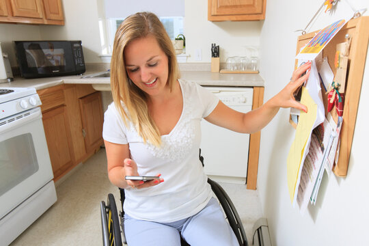 Woman with spinal cord injury in her accessible kitchen looking at her mobile phone