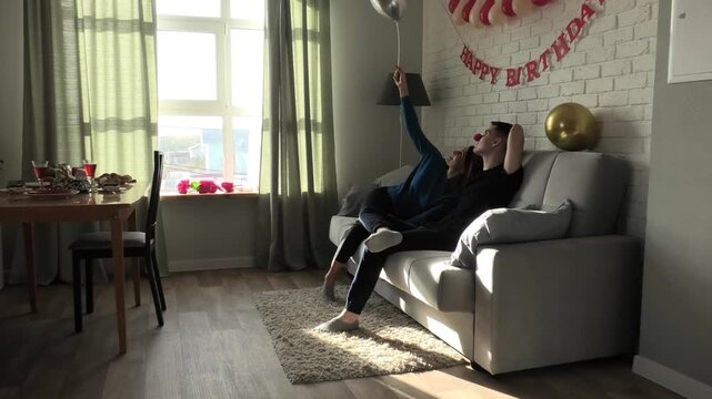 Mother playing with balloon while sitting on sofa with son