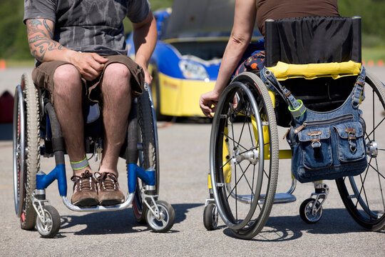 Two disability auto racers on wheelchairs, low section, car in background