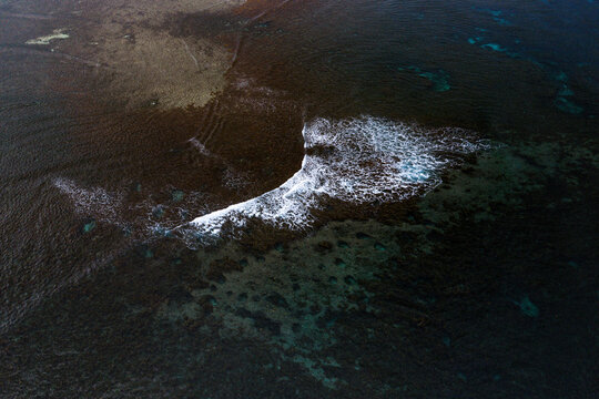 Aerial view of Siargao Island with white waves breaking over the dark coral reef in General Luna, Caraga, Philippines.