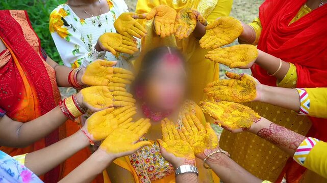 Close-up footage of a traditional Indian Haldi ceremony where family members and friends apply turmeric paste to the bride before marriage. The pre-wedding ritual symbolizes purification, blessings.