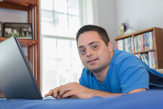 Man with Down Syndrome lying on bed using a laptop