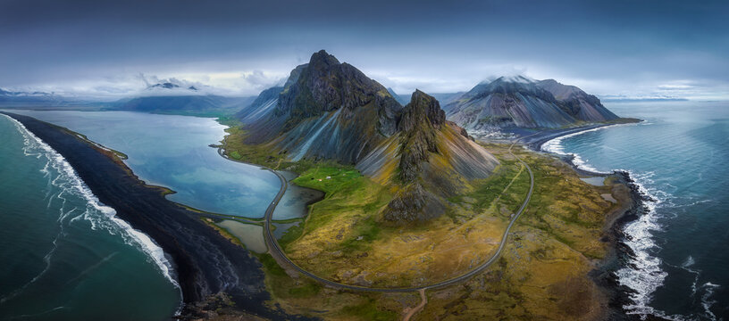 Aerial view of the rugged Hvalnes mountain peaks and a winding road along the black sand coastline Mulathing, Iceland.